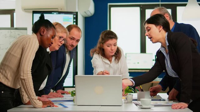 Laptop, collaboration and analysis with business professionals reviewing data and reports around a conference table in a modern office for teamwork, planning, strategy and project decisions.