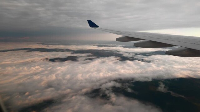 Green forested hills poke through a white layer of low clouds under a grey morning sky seen past an airliner wing during the descent east of Sao Paulo Brazil