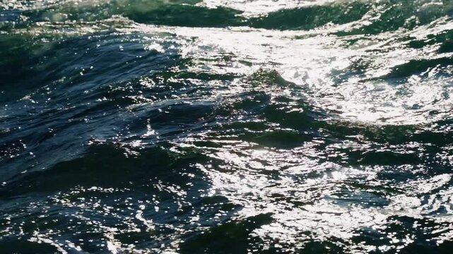 Deep ocean waves churn with sunlight. Ripples catch light, creating dazzling reflections. Water moves powerfully, showing nature's raw energy. Ideal for beach, ocean, or travel visuals