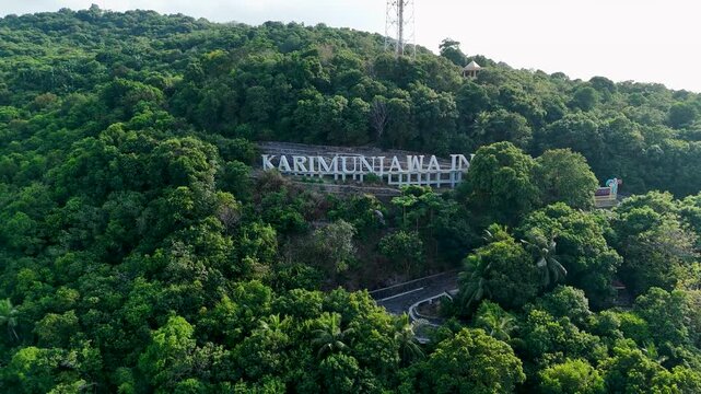 Aerial view of the Karimunjawa sign set on a lush green hillside with dense tropical forest and trees in Karimunjawa, Central Java, Indonesia.
