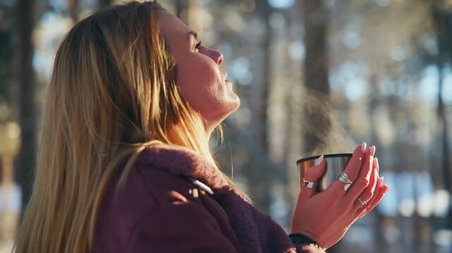 Woman sips steaming drink outdoors. She enjoys quiet moment in snowy woods. Warmth and peace radiate from her. Perfect for winter calm or nature retreat scenes