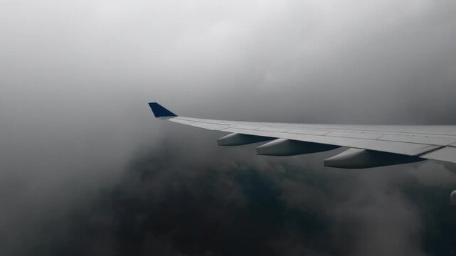 Airliner wing descends through grey clouds with glimpses of green fields and houses below on an overcast morning approach to Guarulhos airport in Sao Paulo Brazil