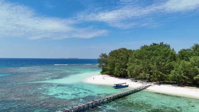 Aerial view of Pulau Cilik featuring a wooden pier extending into clear turquoise waters, a white sandy beach, and lush green trees in Karimunjawa, Central Java, Indonesia.
