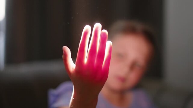 Child's hand glows bright pink against a dim background. Fingers form a shape, glowing warmly as if alive. Soft focus hints at a child's playful imagination. Perfect for scenes of wonder or magic
