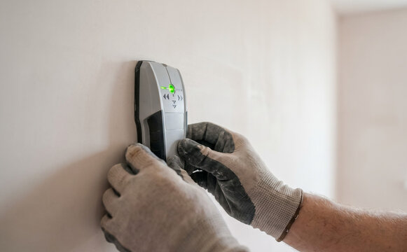 Close-up of a man using a stud finder on a wall during home renovation work