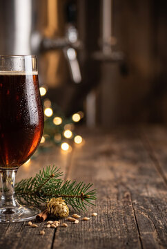 Glass of dark winter ale craft beer on rustic wooden table with pine branch and holiday lights