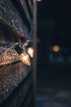 Snowy Christmas string lights glowing on a rustic wooden wall at night for winter holiday backgrounds