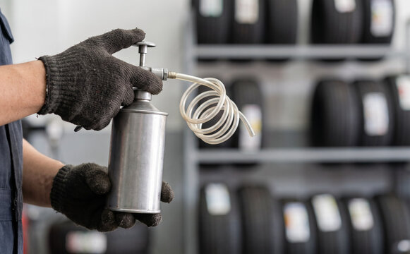 Automotive mechanic holding a pneumatic oil can with a coiled hose in a tire repair service shop