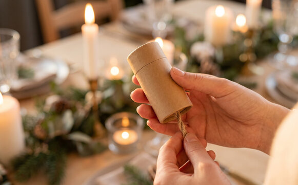 Woman pulling string from kraft paper eco friendly christmas cracker gift tube at festive holiday table setting