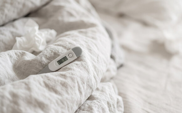 Digital thermometer showing high fever in bed with tissues representing flu, cold, and illness recovery