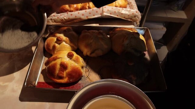 Baker preparing traditional mexican pan de muerto, brushing with glaze and sprinkling with sugar for the day of the dead celebration, showing authentic culinary traditions