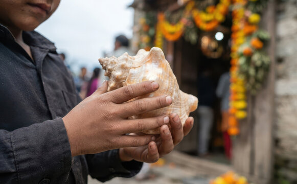 Young boy holding a sacred conch shell outside a decorated Hindu temple