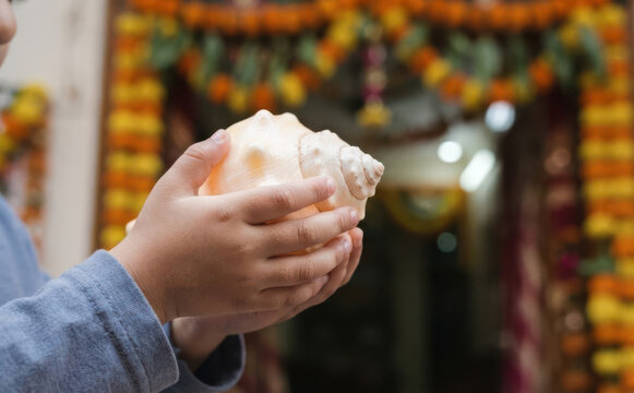 Young South Asian boy holding a large sacred conch shell during a traditional Indian festive celebration