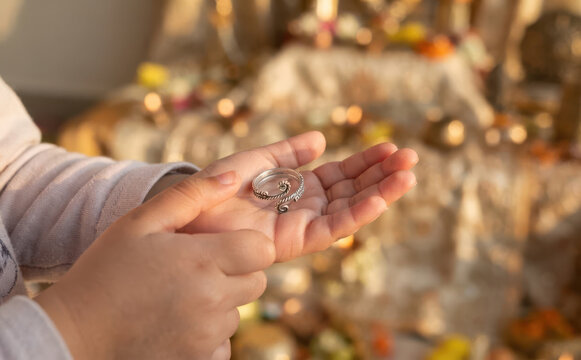 Child hands holding a silver toe ring in palm for traditional Indian rituals and cultural offerings