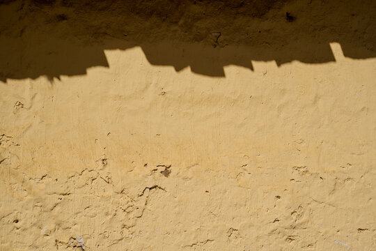 Sombra de tejas proyectada sobre pared r&uacute;stica de adobe amarillo con espacio para texto