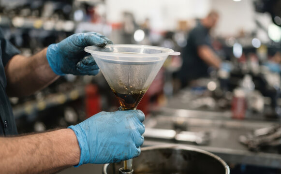 Mechanic filtering dirty motor oil through a plastic funnel in an auto repair shop