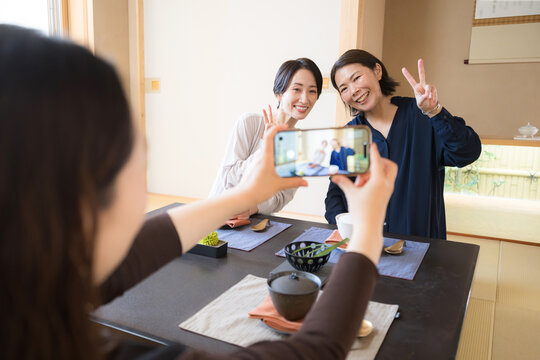 旅館やおしゃれな和食レストランで食事を楽しみながらスマートフォンで記念撮影をする笑顔の日本人女性たち　インスタ映えの旅行イメージ