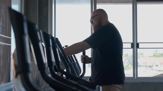 Sport gym workout trainer guides adult man through focused exercise elliptical machine during indoor fitness training, modern cardio equipment, bright urban fitness center, athletic effort