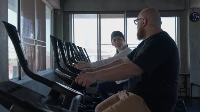 Indoor gym workout with trainer guiding athlete exercise treadmills, elliptical, and rowing machines beside large windows, focused adults sharing energetic fitness, running, sport, and athletic