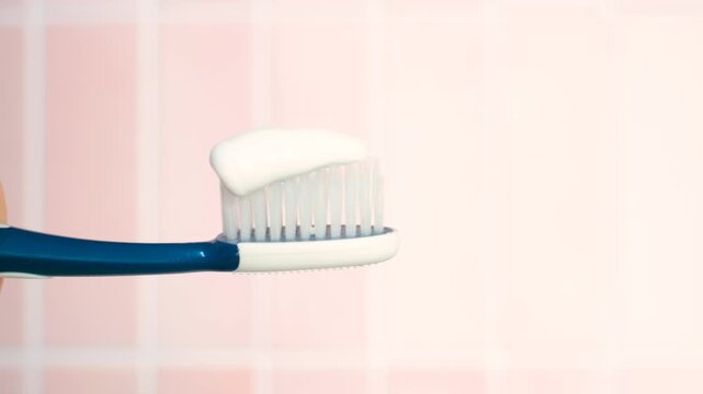 A woman's hand squeezes toothpaste onto a toothbrush on pink background.
