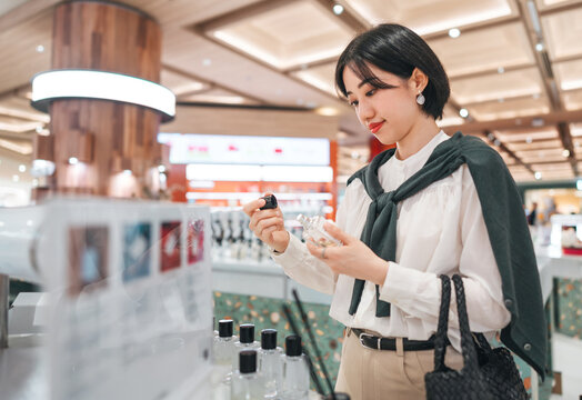 Beautiful smiling asian woman at shopping mall choosing aroma oil fragrance and perfume product
