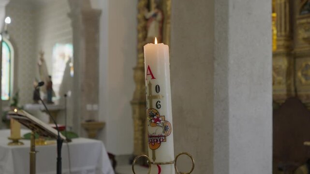 Paschal candle burns near the altar of a Catholic church, decorated with a cross, the Lamb of God and the Greek letters for the beginning and the end