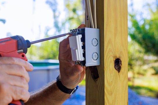 Worker fastening an electrical switch box to wooden post outdoors