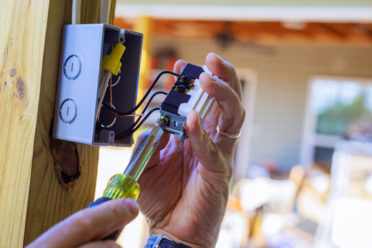 Electrician testing wiring inside wall mounted electrical box during indoor repair work