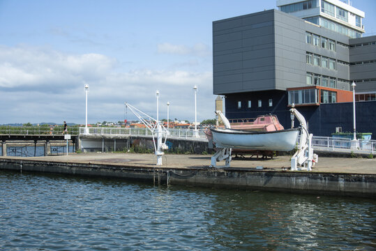 Open lifeboat and davits on the quay in front of a dark modern building