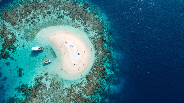 An aerial view of a small sandbar island amidst a coral reef in turquoise waters. Includes space for text (copy space)