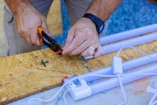 Worker cuts red wire with pliers while repairing fluorescent light fixture outdoors