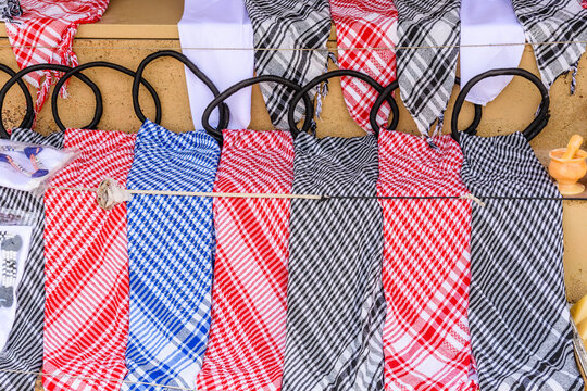 Traditional arabian headdresses and scarves displayed on a marketplace stall featuring various checkered patterns in red white blue and black colors alongside hookah hoses