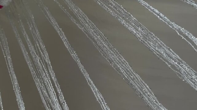 Macro detail of silver metallic string fringe glinting in light, swaying thread curtain decoration, 60fps 4K video