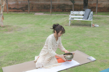 Asian womon practicing meditation with singing bowls on gras © Sirirat Makprasert