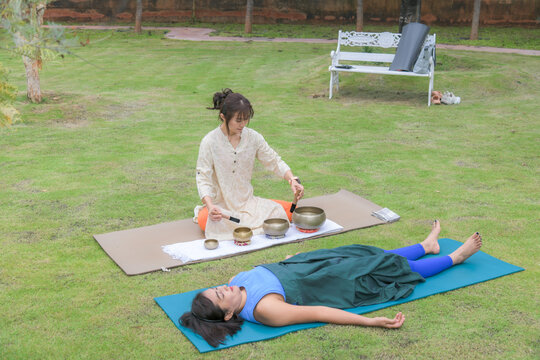 Sound therapist playing singing bowls for woman relaxing in savasana pose