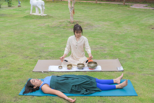 Sound therapist playing singing bowls for woman relaxing in savasana pose