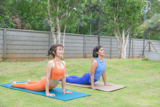 Two women practicing extended side angle yoga pose on mats in a peaceful outdoor garden environment.
