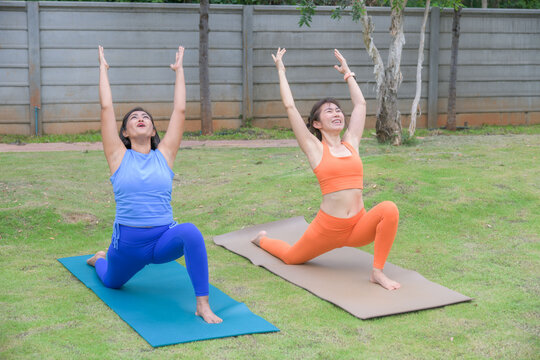 Two women practicing extended side angle yoga pose on mats in a peaceful outdoor garden environment.