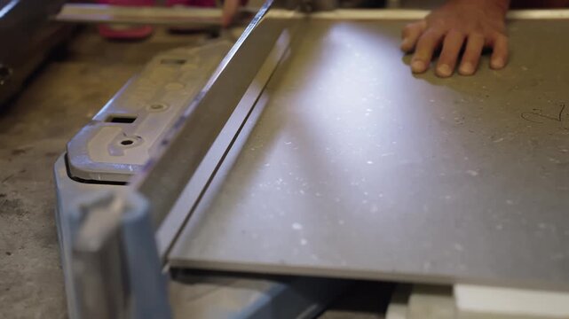 Close-up of a worker positioning a large gray floor tile on a manual rail cutter, aligning the slab for precise scoring and sizing during renovation.