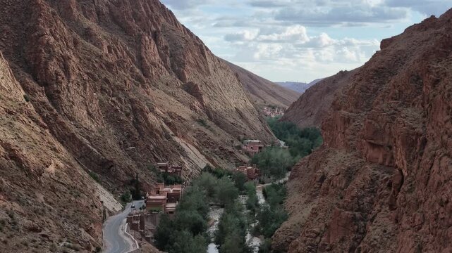 Elevated view of a lush green river valley and scattered traditional settlements nestled between towering canyon walls in Dades Gorge, Morocco