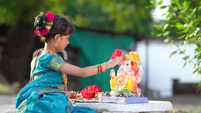 indian little girl doing puja of lord Ganesha sculpture at out of home