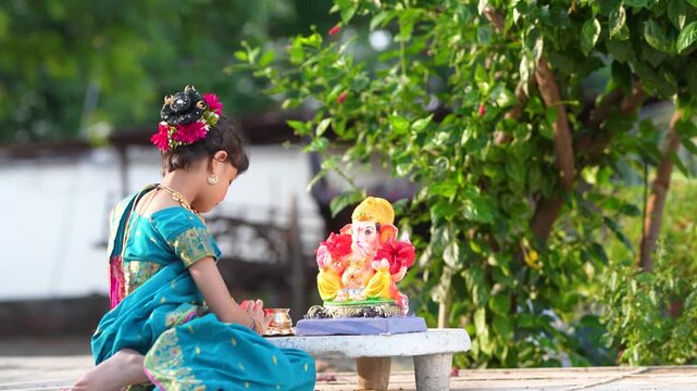 indian little girl doing puja of lord Ganesha sculpture at out of home