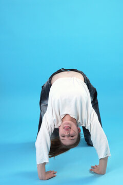 Young Girl Doing Backbend and Sticking Tongue Out on Blue Background