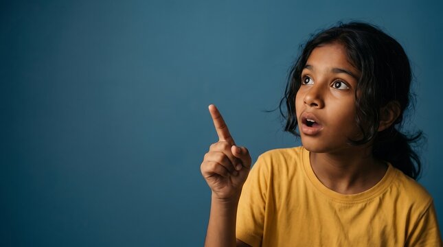 Portrait of a surprised young girl pointing towards copy space on a blue background