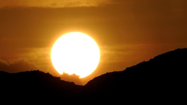 Stuning silhouette of dark mountains against a bright glowing sun during sunset or sunrise, creating a dramatic and serene natural landscape view.