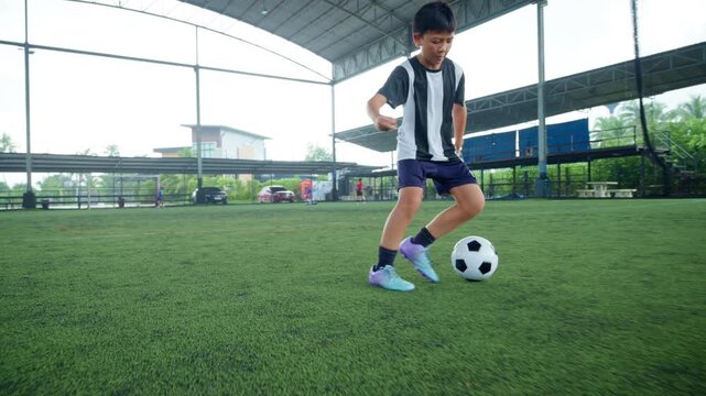 Close-up of a boy kicking a soccer ball on a green turf field, with sharp detail and frozen motion, representing youth sports, training, fitness and a healthy active lifestyle.