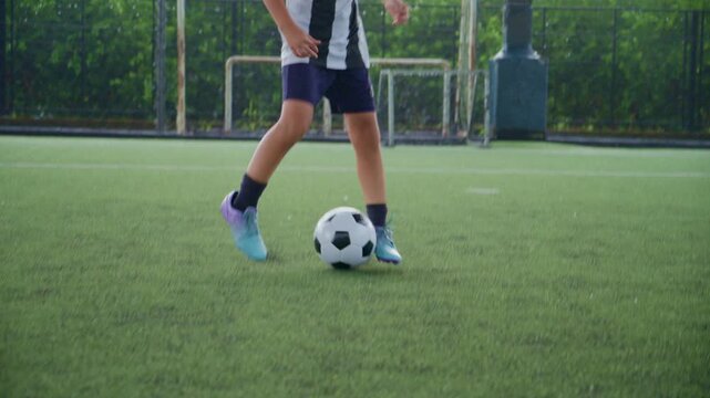 Close-up of a boy kicking a soccer ball on a green turf field, with sharp detail and frozen motion, representing youth sports, training, fitness and a healthy active lifestyle.