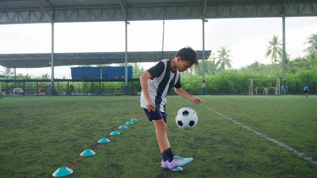 Close-up of a boy kicking a soccer ball on a green turf field, with sharp detail and frozen motion, representing youth sports, training, fitness and a healthy active lifestyle.