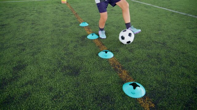 Close-up of a boy kicking a soccer ball on a green turf field, with sharp detail and frozen motion, representing youth sports, training, fitness and a healthy active lifestyle.