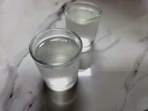 Two shot glasses of fresh coconut water on white marble table, clear refreshing natural tropical drink